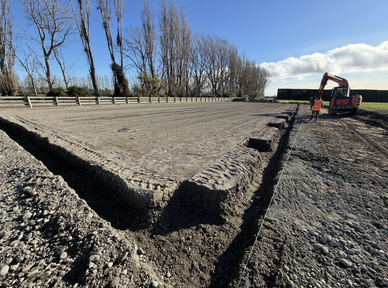 Prepared foundation pad with perimeter footing excavation, excavator and worker